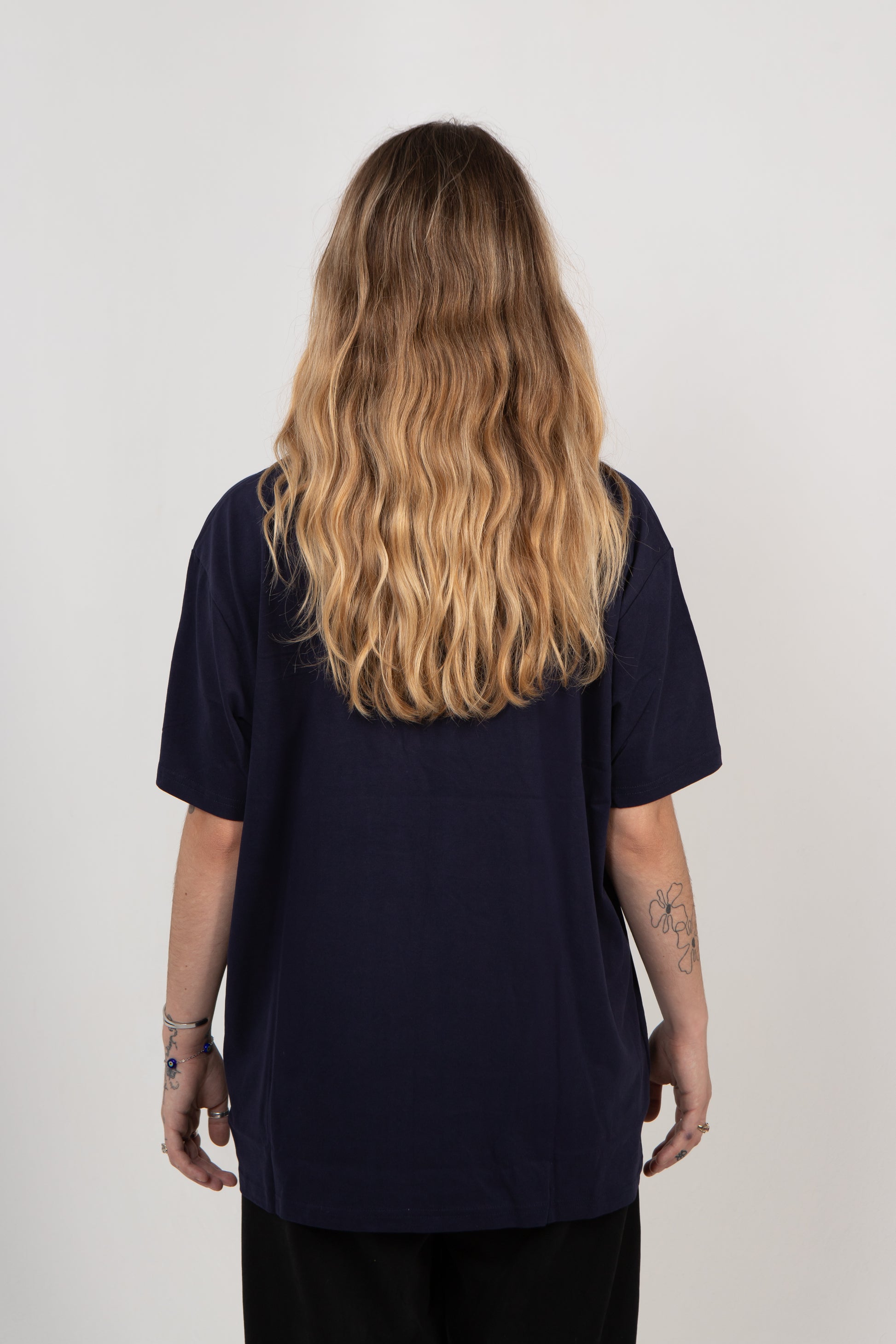 Person wearing a navy blue t-shirt with long wavy hair on a plain background