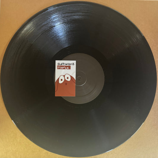 A vinyl record labeled 'Awkward Silence' with a barcode and partially visible text, placed on a wooden surface.