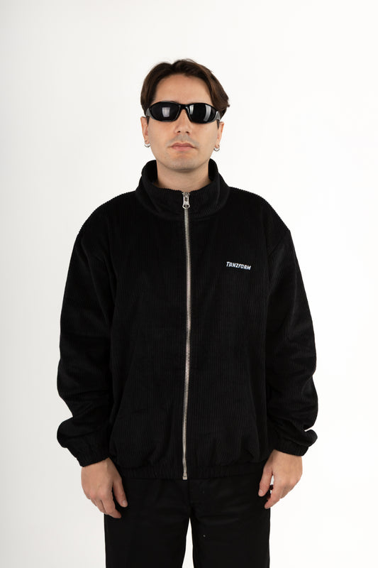 Person wearing a black corduroy jacket with a brand logo on a white background