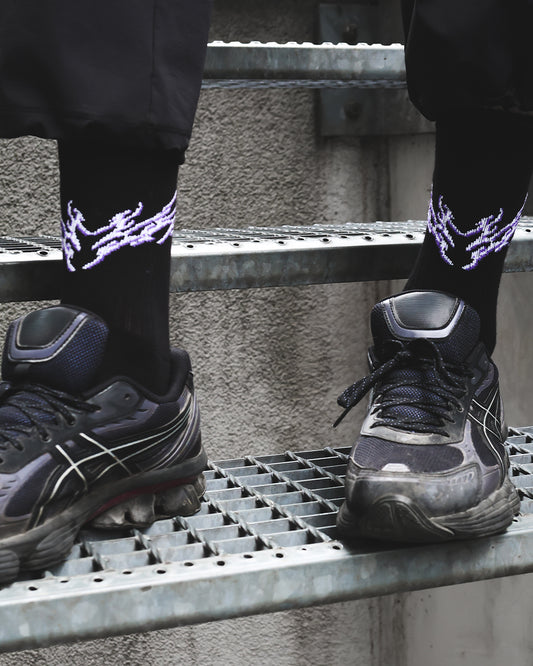 Person wearing black shoes and socks with glowing purple designs on a metal stairs.