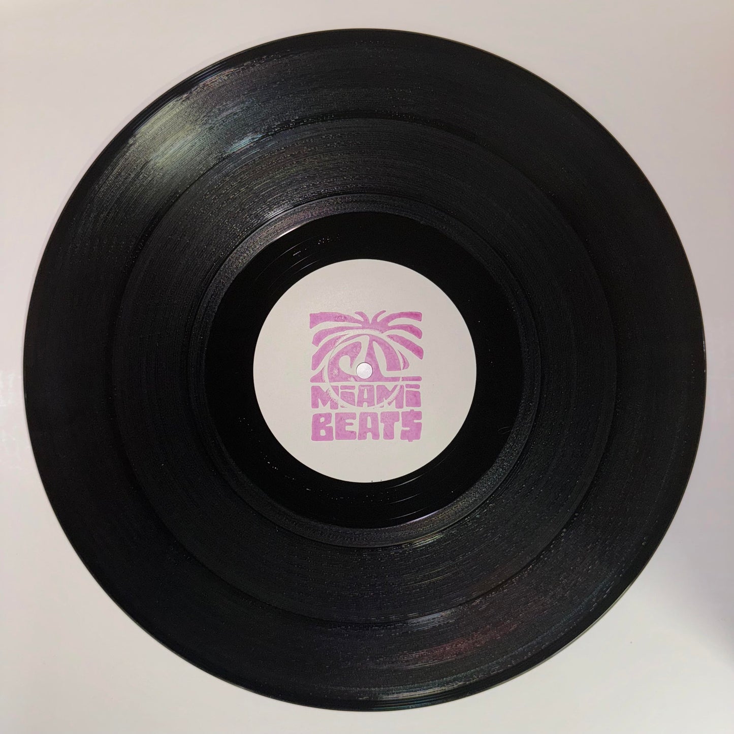 A vinyl record with 'Miami Beat$' label featuring a pink logo on a white label record.