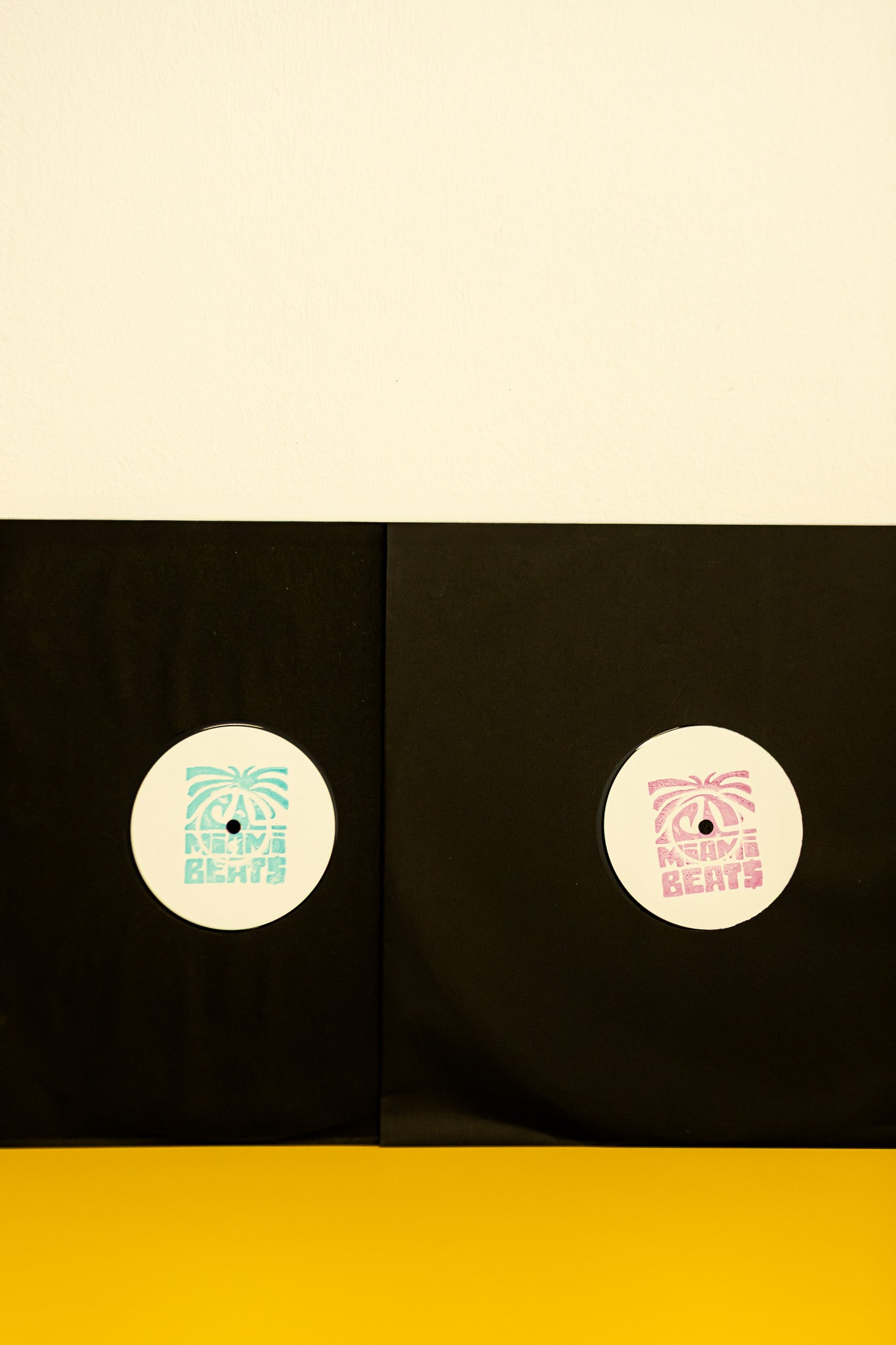 Two vinyl records with white labels on a black background, with a beige top and yellow bottom.