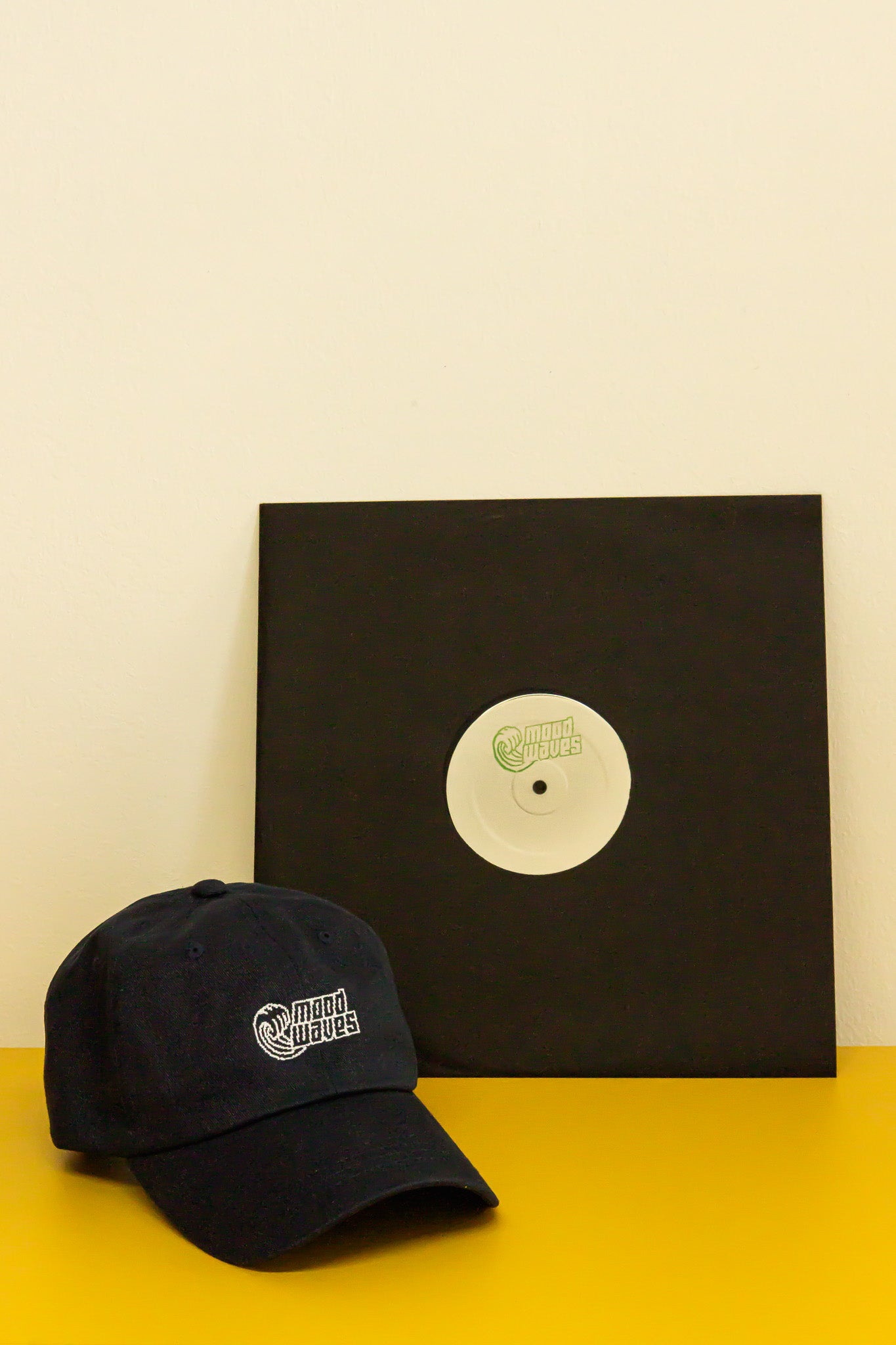 Black cap and vinyl record with a black cover on a yellow surface