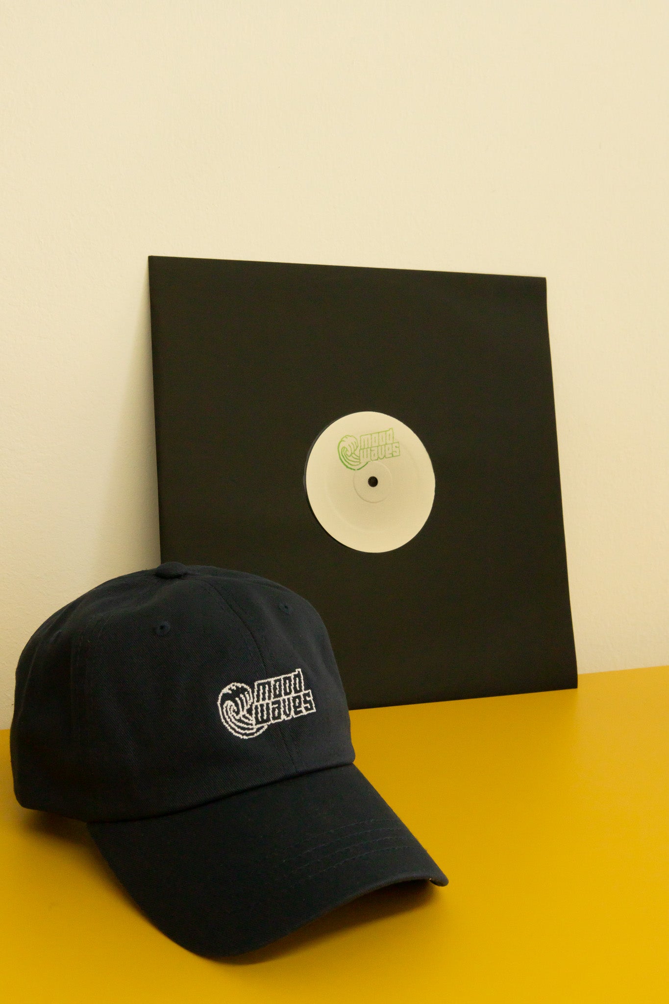 Black cap with a logo and a vinyl record on a yellow surface