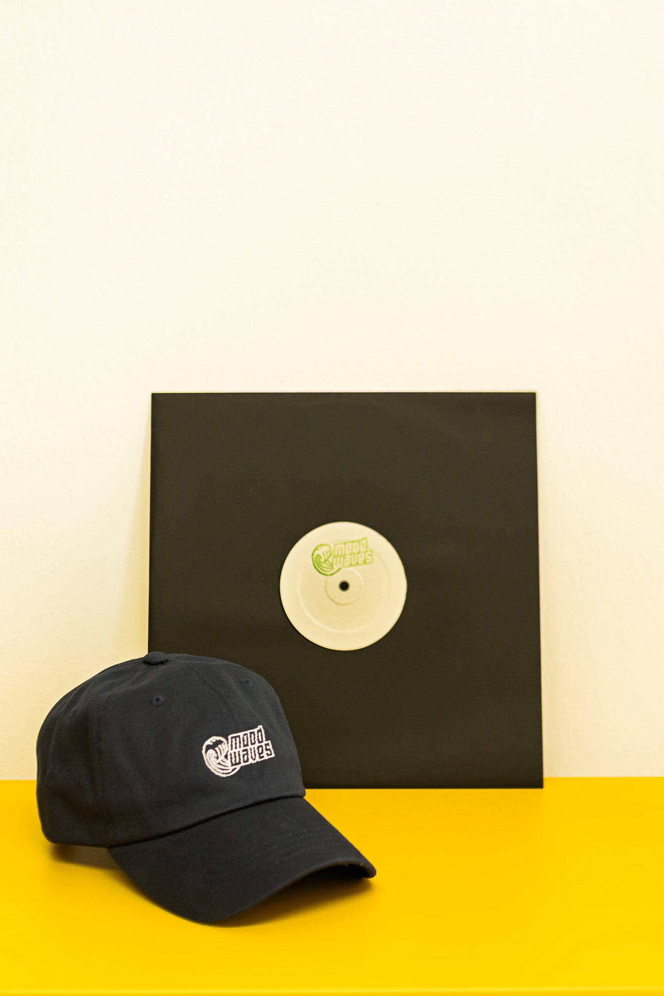 Black cap and vinyl record with a logo on a yellow surface and beige background