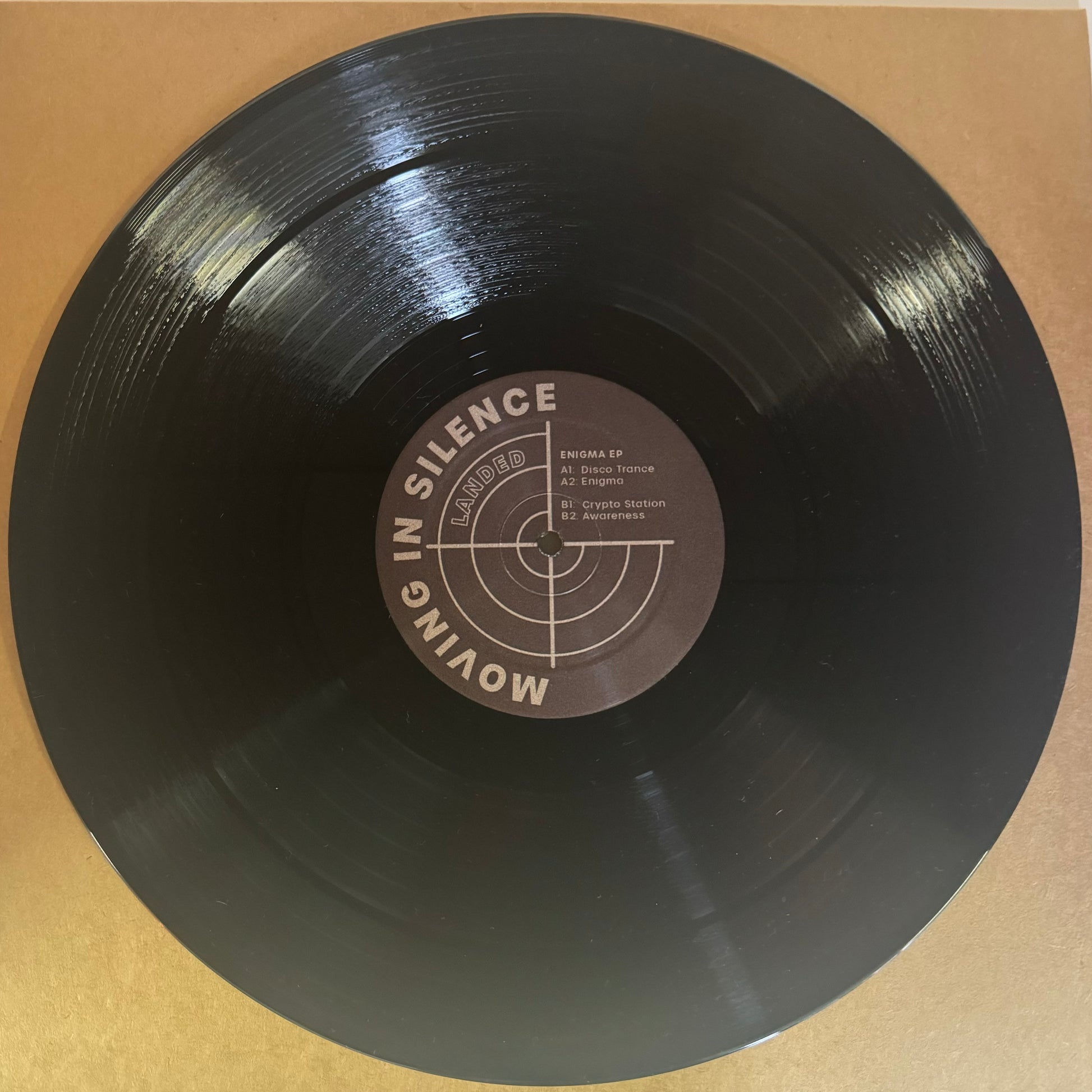 A black vinyl record labeled 'Moving In Silence' with a central label featuring text and the title 'Enigma EP'.