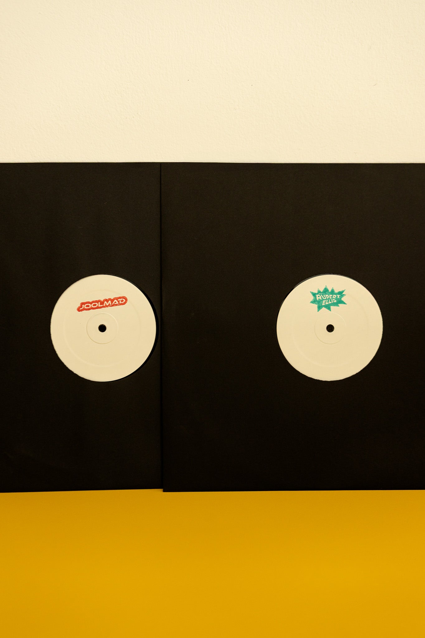 Two vinyl records with labels on a black sleeve against a beige background
