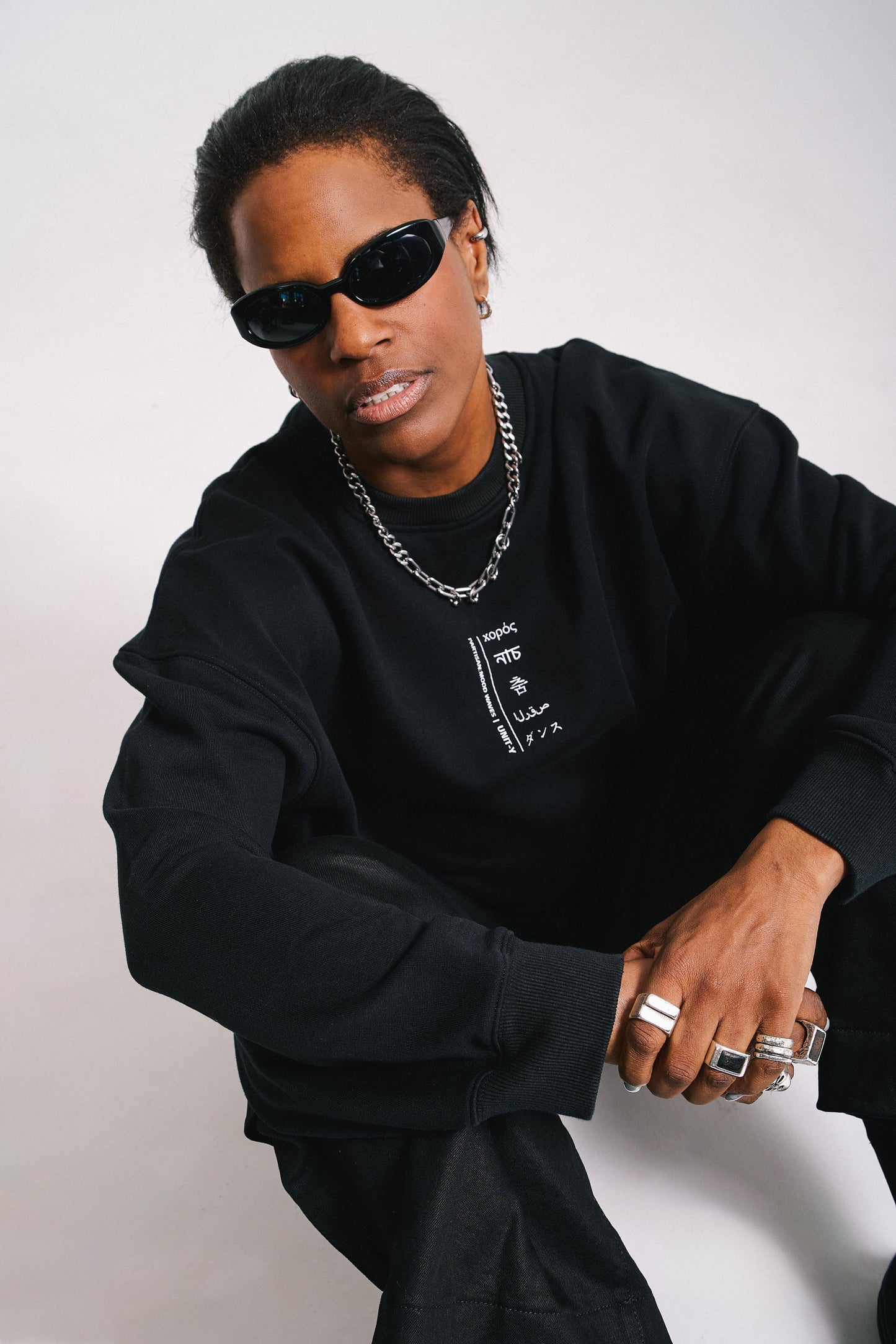 A person wearing a black Unit-Y sweater with extra wide sleeves, paired with sunglasses and a necklace.