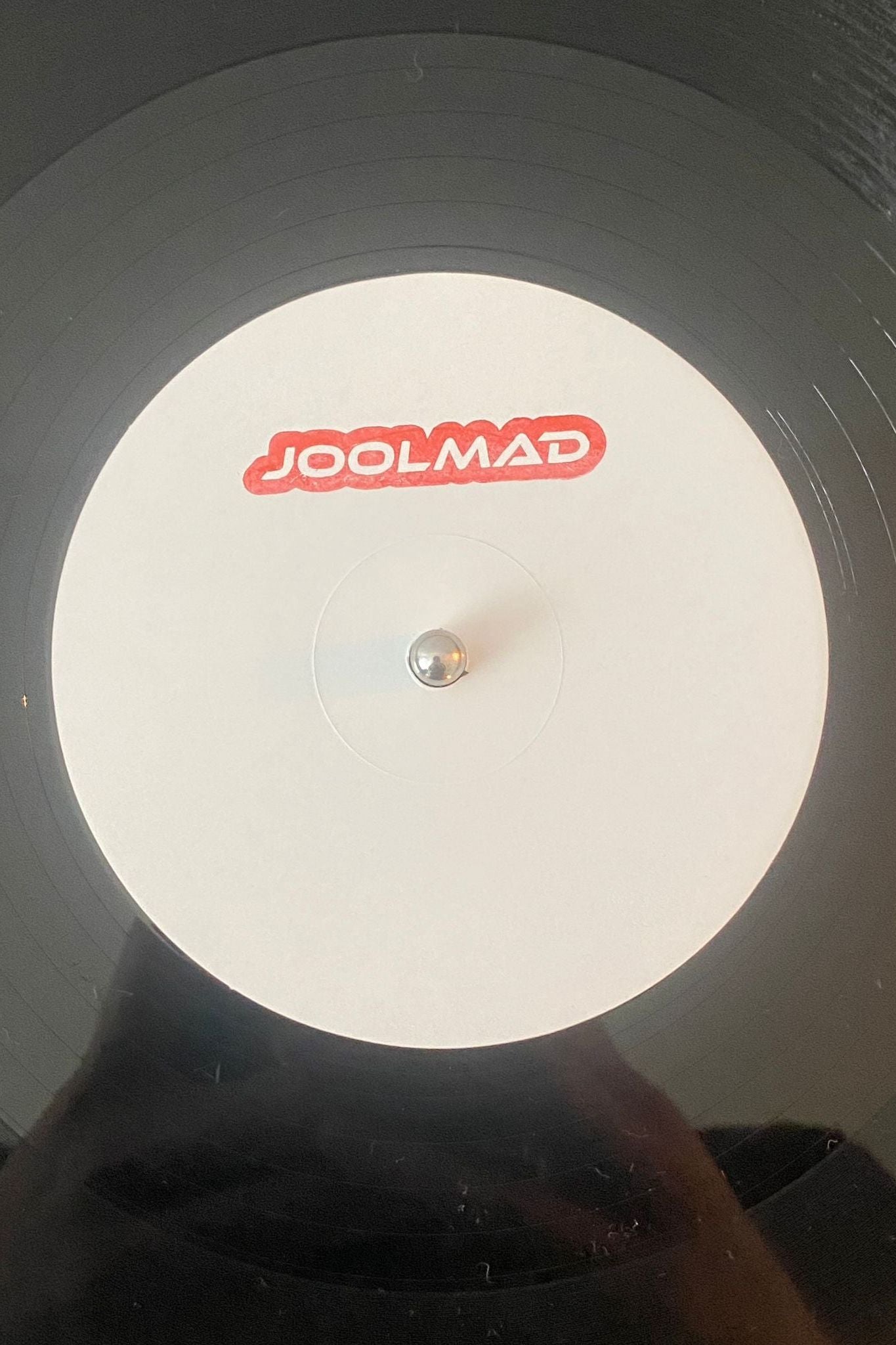 A vinyl record with a white label featuring the text 'JOOLMAD' in the center, placed on a dark background.