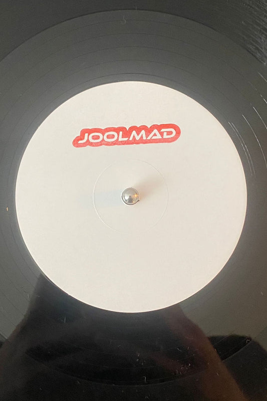 A vinyl record with a white label featuring the text 'JOOLMAD' in the center, placed on a dark background.
