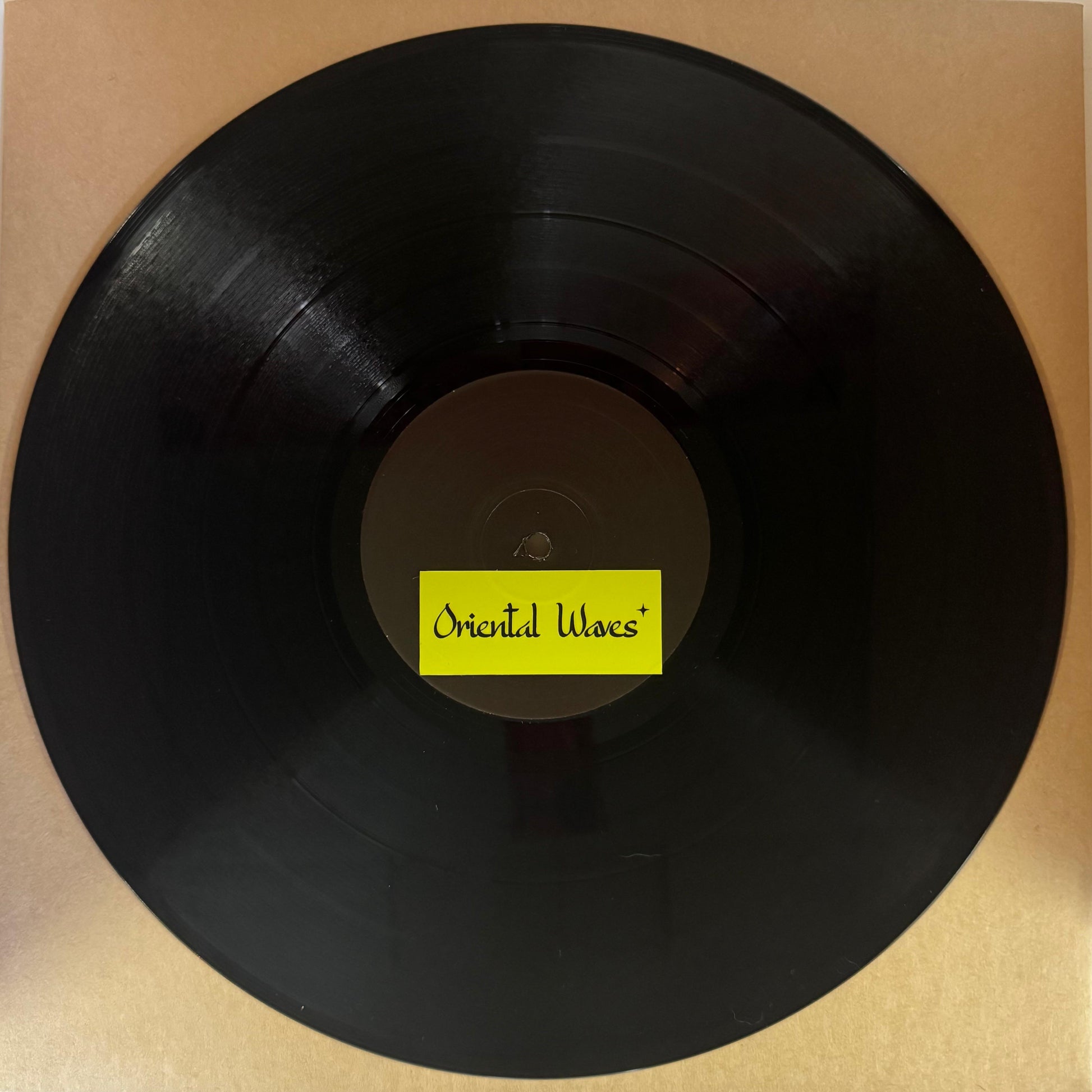 Vinyl record with a yellow label saying oriental waves on a cardboard background