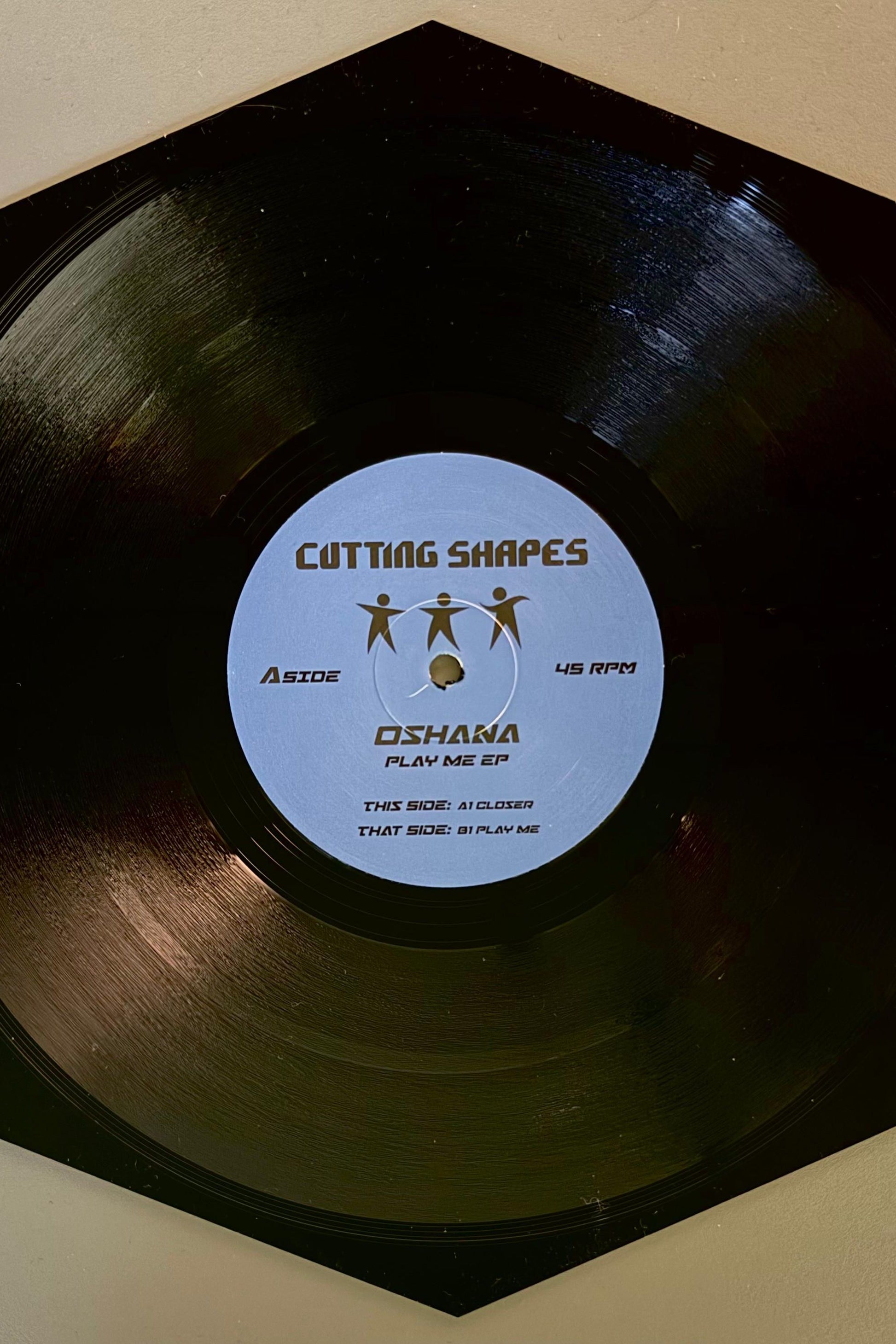 A black vinyl record labeled 'Cutting Shapes' with 'Oshana - Play Me EP' in the center.