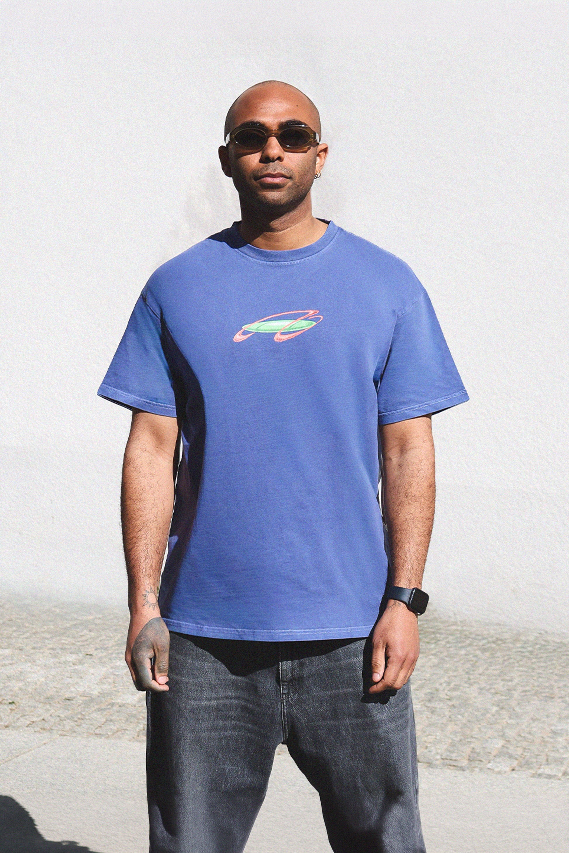 Lawrence Asher wearing a blue t-shirt with a colorful graphic design against a plain background