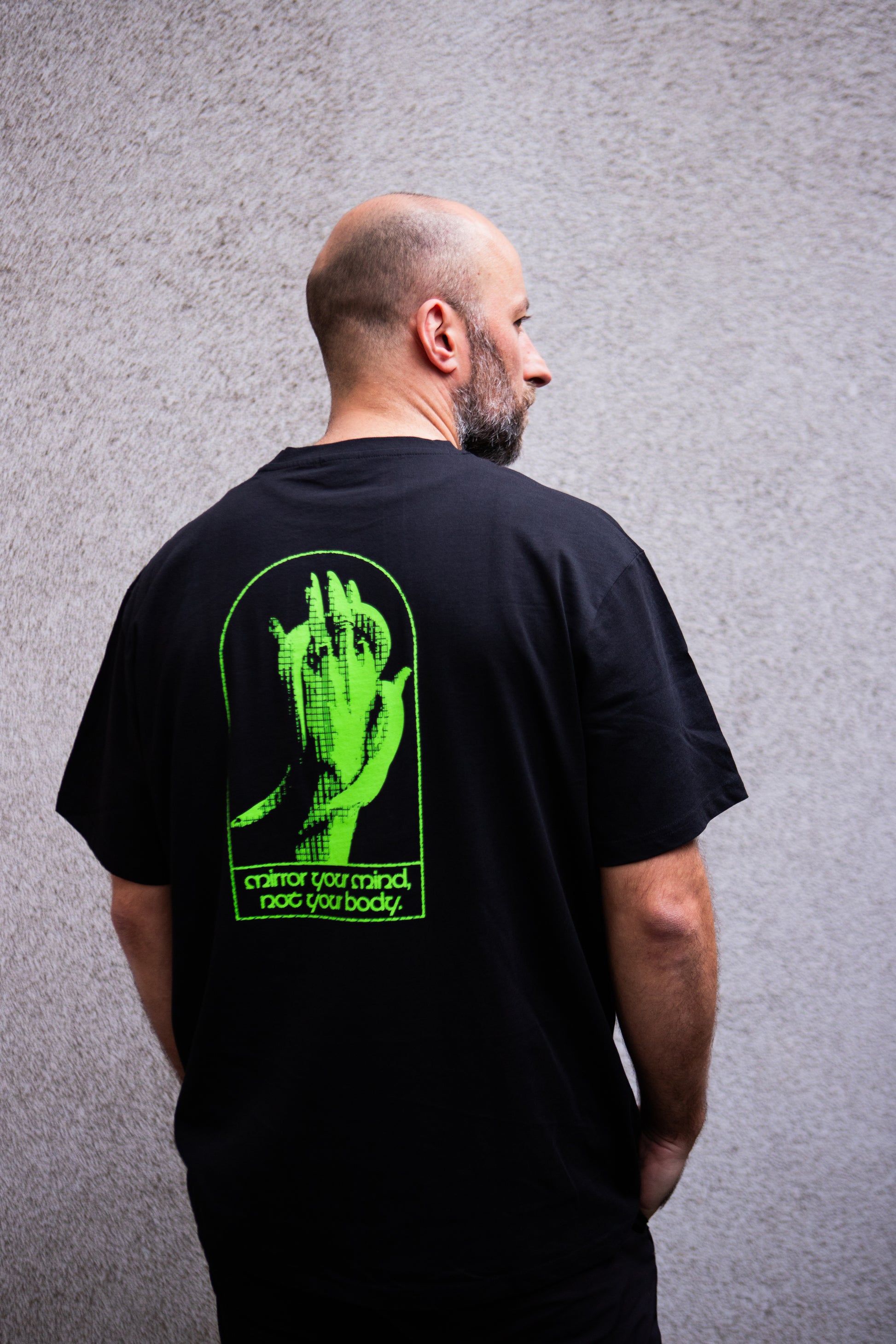 Man wearing a black t-shirt with a green graphic on the back against a gray background