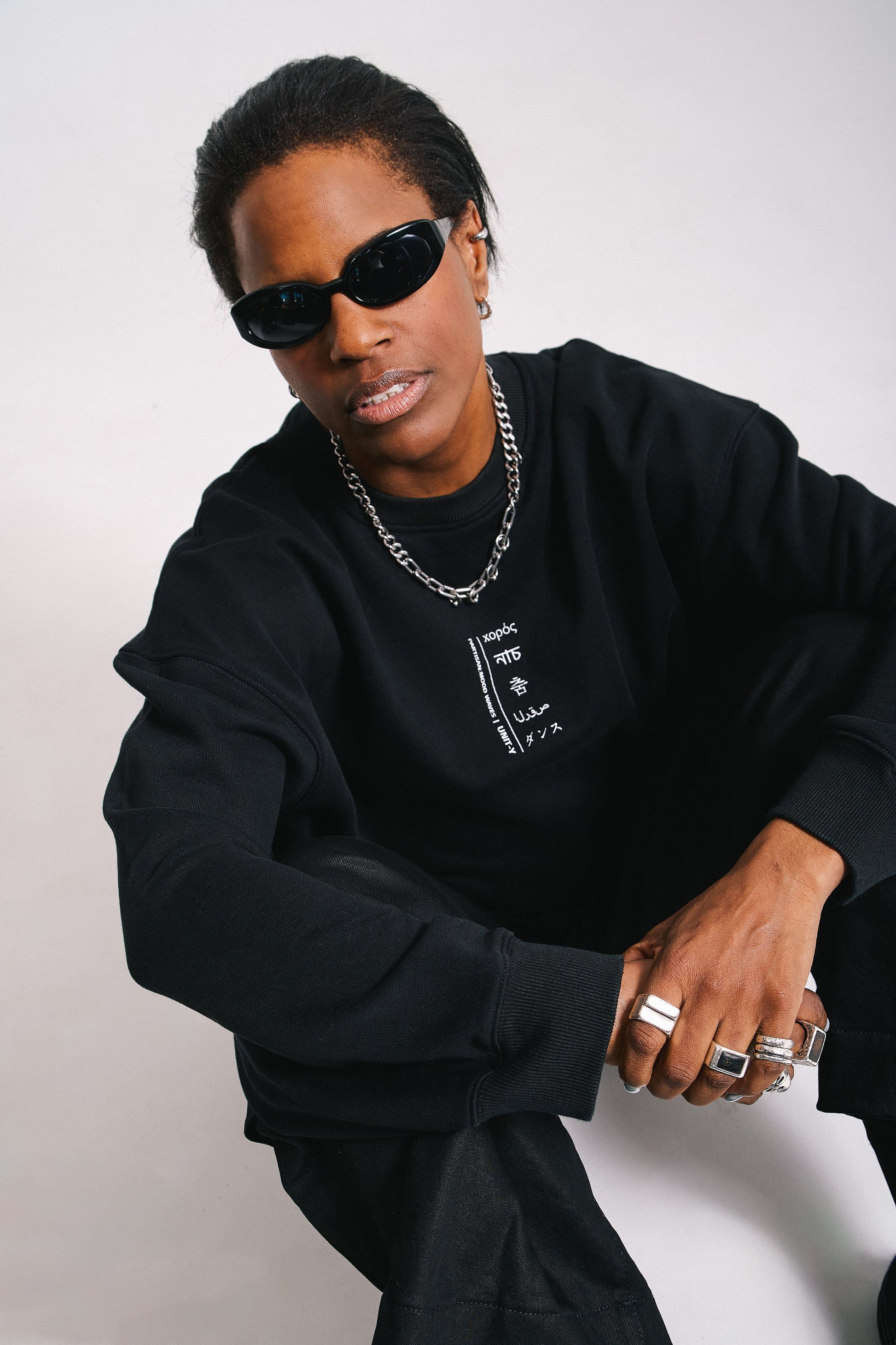 A person wearing a black Unit-Y sweater with extra wide sleeves, paired with sunglasses and a necklace.