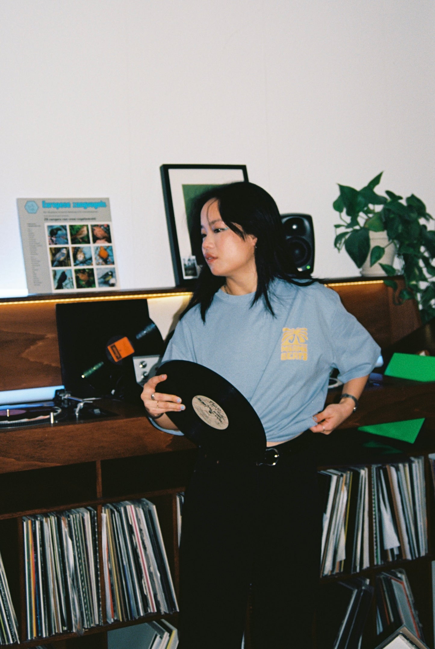 helly wearing a miami beats tshirt and holding a record in her hand in front of a dj booth