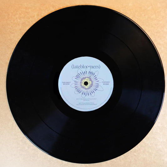 A black vinyl record with a white center label reading 'latebloomers' and a purple flower graphic, photographed from above on a beige textured background.
